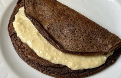 Fotografia de uma panqueca de chocolate com recheio de coco cremoso sobre um prato branco de vidro. Fotografia de uma panqueca de chocolate com recheio de coco cremoso sobre um prato branco de vidro.