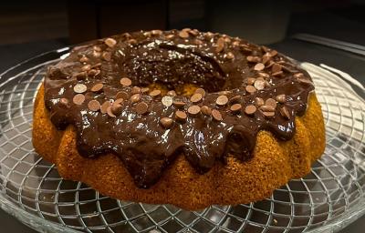 Foto da receita de Bolo de cenoura e especiarias sem glúten. Observa-se um bolo com furo no meio fofinho com uma calda brilhante de chocolate decorado com gotas. Foto da receita de Bolo de cenoura e especiarias sem glúten. Observa-se um bolo com furo no meio fofinho com uma calda brilhante de chocolate decorado com gotas.