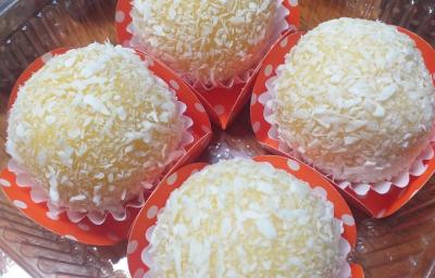 Foto da receita de brigadeiro de milho verde. Observa-se 4 unidades de brigadeiro em forminhas laranjas com estampa de poá branca.