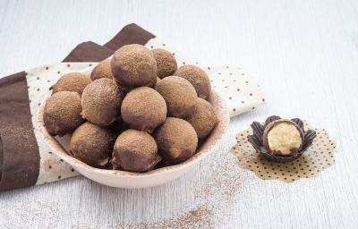 foto em tons de marrom, branco e rosa de uma bancada vista de cima. Contém um recipiente redondo cor rosa com trufas de chocolate e abaixo um pano marrom e um pano branco com bolinhas marrom. Ao lado uma trufa pela metade em uma forminha preta foto em tons de marrom, branco e rosa de uma bancada vista de cima. Contém um recipiente redondo cor rosa com trufas de chocolate e abaixo um pano marrom e um pano branco com bolinhas marrom. Ao lado uma trufa pela metade em uma forminha preta