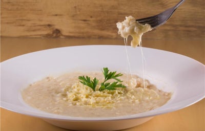 Foto da receita de risoto quatro queijos tirolez, servida em um prato fundo branco, com um garfo puxando um punhado e mostrando o queijo derretido
