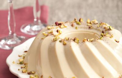 fotografia em tons de cinza e bege vista de frente, contém um prato redondo branco com um Flan de pistache e ao lado duas taças transparentes, abaixo um pano cor vinho fotografia em tons de cinza e bege vista de frente, contém um prato redondo branco com um Flan de pistache e ao lado duas taças transparentes, abaixo um pano cor vinho