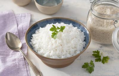 Fotografia em tons de lilás em uma bancada de madeira clara, um pano lilás e um pote marrom redondo fundo com o arroz basmati dentro dele. Ao lado, um pote hermético com arroz cru e uma colher de servir. Fotografia em tons de lilás em uma bancada de madeira clara, um pano lilás e um pote marrom redondo fundo com o arroz basmati dentro dele. Ao lado, um pote hermético com arroz cru e uma colher de servir.