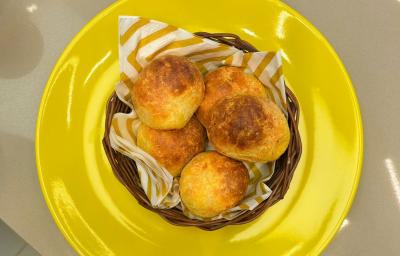 Fotografia em tons de amarelo com um prato amarelo ao centro. Dentro do prato existe uma cestinha com vários pãezinhos feito com queijo e Ninho Adulto Fotografia em tons de amarelo com um prato amarelo ao centro. Dentro do prato existe uma cestinha com vários pãezinhos feito com queijo e Ninho Adulto