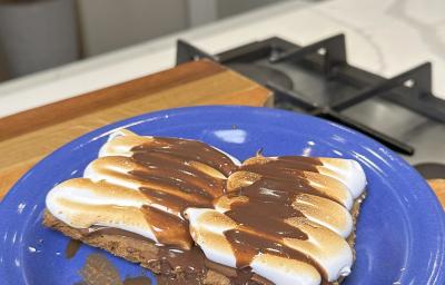 Fotografia de uma receita de smores com cookie em um prato de vidro raso sobre uma tábau de madeira.
