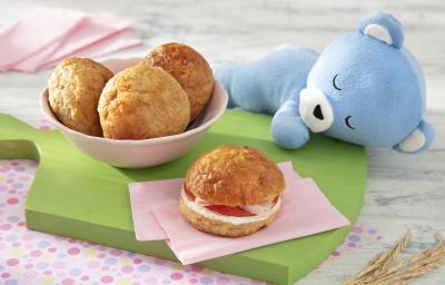 Foto da receita de Pão de Leite. Observa-se um potinho rosa com três pãezinhos e, ao lado direito, um pão com recheio de tomate, requeijão e peito de peru, sobre uma tábua verde. Foto da receita de Pão de Leite. Observa-se um potinho rosa com três pãezinhos e, ao lado direito, um pão com recheio de tomate, requeijão e peito de peru, sobre uma tábua verde.