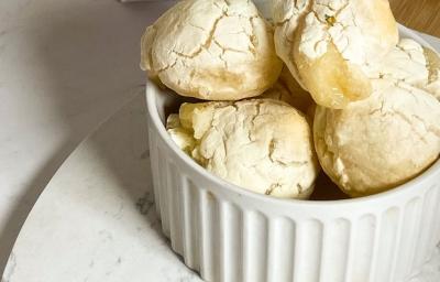 Foto da receita de pão de queijo vegano servida em diversas porções em um prato de porcelana branca sobre uma tábua de madeira. Foto da receita de pão de queijo vegano servida em diversas porções em um prato de porcelana branca sobre uma tábua de madeira.