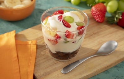 Fotografia mostra uma taça de pavê com camadas visíveis de creme branco, frutas coloridas e pedaços de biscoito integral, formando um visual fresco e apetitoso.