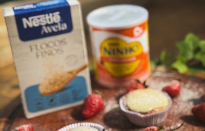 Fotograifa em tons claros da receita sob o sol de três muffins em forminha de papel sobre uma tábua grande e redonda de madeira. Tem ao lado dos muffins alguns morangos inteiros com leite ninho polvilhado. Fotograifa em tons claros da receita sob o sol de três muffins em forminha de papel sobre uma tábua grande e redonda de madeira. Tem ao lado dos muffins alguns morangos inteiros com leite ninho polvilhado.