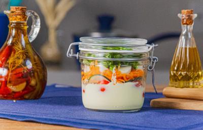 Fotografia em tons de azul com um pote de vidro ao centro. Dentro do pote existe uma receita de salada rúcula com cenoura, pepino, tomate cereja com molho caesar Fotografia em tons de azul com um pote de vidro ao centro. Dentro do pote existe uma receita de salada rúcula com cenoura, pepino, tomate cereja com molho caesar
