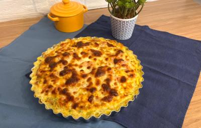 Fotografia em tons de azul com uma forma ao centro. Dentro da forma existe uma receita de quiche com massa de batata gratinada.