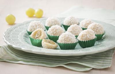 Fotografia em tons de verde e branco de uma bancada vista de frente, contém um pano listrado em verde e branco, um prato redondo branco com vários beijinhos em forma de bolinha com coco por cima.