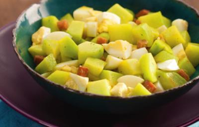 Fotografia em tons de verde e vinho, com saladeira em verde ao centro com chuchu, bacon e ovo cozidos, sobre prato cor vinho e guardanapo azul, sobre bancada marrom. Fotografia em tons de verde e vinho, com saladeira em verde ao centro com chuchu, bacon e ovo cozidos, sobre prato cor vinho e guardanapo azul, sobre bancada marrom.