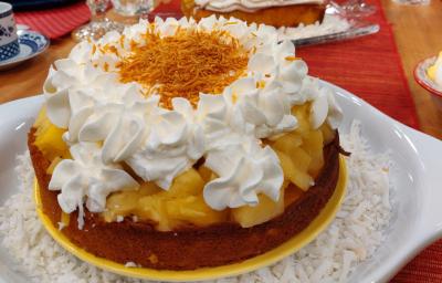 Foto aproximada da receita de bolo de pina colada com leite moça, um doce servido em um prato branco e amarelo, em camadas de massa, abacaxi picado, merengue decorado e coco ralado por cima.