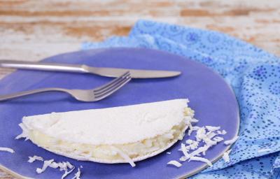 Fotografia em tons de azul em uma bancada de madeira clara, um pano azul, um prato azul redondo com uma tapioca de coco em cima dele. Fotografia em tons de azul em uma bancada de madeira clara, um pano azul, um prato azul redondo com uma tapioca de coco em cima dele.