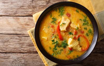 fotografia em tons de marrom e amarelo de uma bancada marrom vista de cima. Contém um pano amarelo com um recipiente redondo preto com pedaços de peixe e pimentão.