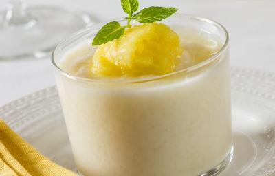 Fotografia de um recipiente pequeno transparente com um strogonoff doce de abacaxi gelado, com alguns pedaços sobre o creme. O recipiente está sobre um prato raso branco. Fotografia de um recipiente pequeno transparente com um strogonoff doce de abacaxi gelado, com alguns pedaços sobre o creme. O recipiente está sobre um prato raso branco.