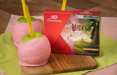 Imagem de duas maçãs do amor cobertas com chocolate rosa. Ao lado, uma caixinha do chocolate Wicked. Imagem de duas maçãs do amor cobertas com chocolate rosa. Ao lado, uma caixinha do chocolate Wicked.