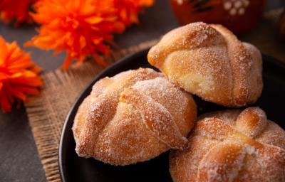 Fotografia de três unidades de pãezinhos recheados com doce de leite e passados na canela e no açúcar, os quais estão dentro de um recipiente preto fundo. Fotografia de três unidades de pãezinhos recheados com doce de leite e passados na canela e no açúcar, os quais estão dentro de um recipiente preto fundo.