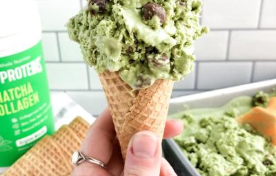 Fotografia em tons de verde em uma bancada de madeira, com um fundo de azulejo, com uma pessoa segurando uma casquinha com o sorvete de matcha, um pote de produto de Vital Proteins. E ao fundo, um recipiente com mais sorvete. Fotografia em tons de verde em uma bancada de madeira, com um fundo de azulejo, com uma pessoa segurando uma casquinha com o sorvete de matcha, um pote de produto de Vital Proteins. E ao fundo, um recipiente com mais sorvete.