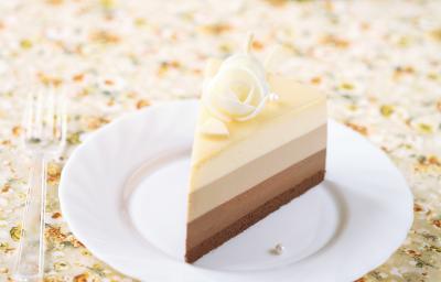 Fotografia de tons claros de uma torta diplomata, com creme preto e branco em camadas em um prato branco de sobremesa. Ao lado, um garfo pequeno de plástico sobre uma toalha de mesa colorida. Fotografia de tons claros de uma torta diplomata, com creme preto e branco em camadas em um prato branco de sobremesa. Ao lado, um garfo pequeno de plástico sobre uma toalha de mesa colorida.