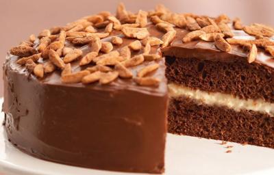 Fotografia em tons de rosa em uma mesa com uma toalha bege, um guardanapo de pano rosinha, um suporte para bolo branco com o bolo de chocolate cortado ao meio em cima dele. Fotografia em tons de rosa em uma mesa com uma toalha bege, um guardanapo de pano rosinha, um suporte para bolo branco com o bolo de chocolate cortado ao meio em cima dele.