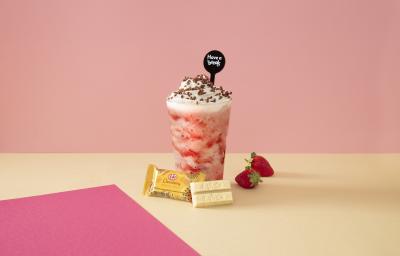 Foto em tons de cor de rosa da receita de smoothie de morango servida sobre uma mesa amarela com kit kat amarelo à frente Foto em tons de cor de rosa da receita de smoothie de morango servida sobre uma mesa amarela com kit kat amarelo à frente