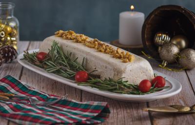 Foto da receita de Mousse de Queijos, num prato branco, sobre uma bancada de madeira toda decorada com motivos natalinos, uma vez branca acesa ao fundo e um tecido colorido de natal como guardanapo