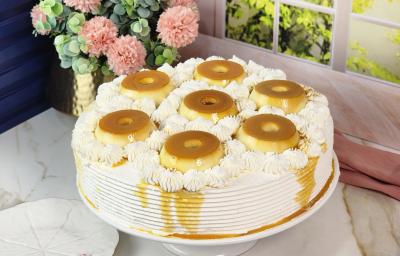 Foto da Receita de Bolo Recheado de Pudim com Doce de Leite Moça, decorado sobre um prato branco com sete mini pudins por cima, em uma bancada de mármore com flores ao fundo Foto da Receita de Bolo Recheado de Pudim com Doce de Leite Moça, decorado sobre um prato branco com sete mini pudins por cima, em uma bancada de mármore com flores ao fundo