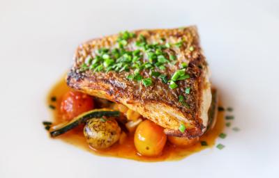 Fotografia de um filé de pescado ao papillote com alguns legumes ao forno por baixo do peixe. Por cima do peixe, que está em um prato branco, tem cebolinha salpicada. Fotografia de um filé de pescado ao papillote com alguns legumes ao forno por baixo do peixe. Por cima do peixe, que está em um prato branco, tem cebolinha salpicada.