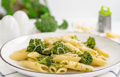 fotografia em tons de branco, bege e verde vista de frente. Contém um prato redondo branco com macarrão tipo penne e brócolis fotografia em tons de branco, bege e verde vista de frente. Contém um prato redondo branco com macarrão tipo penne e brócolis