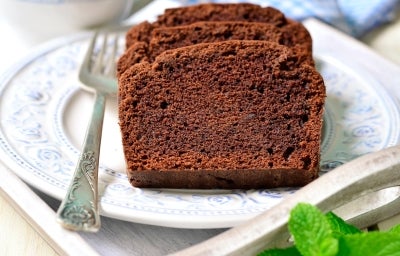 Fatias de bolo de chocolate fofinho em um prato decorado com flores azuis. Um garfo prateado ao lado e uma folha de hortelã adicionam charme. O fundo desfocado com um pano xadrez cria uma atmosfera acolhedora. Fatias de bolo de chocolate fofinho em um prato decorado com flores azuis. Um garfo prateado ao lado e uma folha de hortelã adicionam charme. O fundo desfocado com um pano xadrez cria uma atmosfera acolhedora.