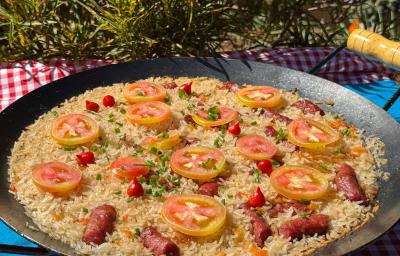 Fotografia de um tacho de ferro fundo com uma receita de arroz com calabresa decorada com tomate em rodelas e pimenta biquinho. Fotografia de um tacho de ferro fundo com uma receita de arroz com calabresa decorada com tomate em rodelas e pimenta biquinho.