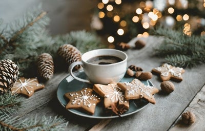 Em cima de uma mesa decorada pinhas e árvore de Natal, prato com três biscoitos em forma de estrela, decorados com açúcar de confeiteiro.