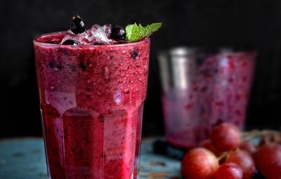 Fotografia em tom escuro de dois copos de vidro, o da frente está cheio com uma bebida de suco de uva com leite e neston, e o do fundo está quase vazio. Fotografia em tom escuro de dois copos de vidro, o da frente está cheio com uma bebida de suco de uva com leite e neston, e o do fundo está quase vazio.
