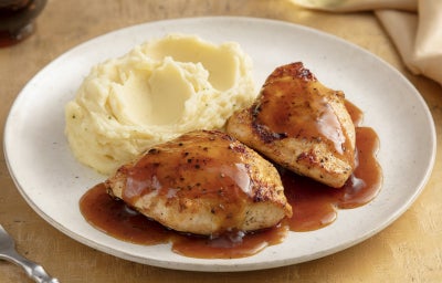 Pedaços de frango dourados servidos com purê cremoso de batata e molho escuro reduzido, apresentados em prato branco elegante