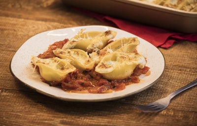 Foto da receita de Conchiglione recheado com 3 queijos Tirolez, servidos lado a lado em um prato branco. Eles estão recheados e cobertos com mais queijo, sobre um molho rústico de tomate