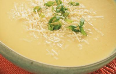 Fotografia em tons de creme e vermelho, com refratário cinza ao centro contendo um creme amarelo decorado com queijo e cebolinha picada sobre guardanapo vermelho, com colher ao lado e tudo sobre aparador de palha na cor bege. Fotografia em tons de creme e vermelho, com refratário cinza ao centro contendo um creme amarelo decorado com queijo e cebolinha picada sobre guardanapo vermelho, com colher ao lado e tudo sobre aparador de palha na cor bege.