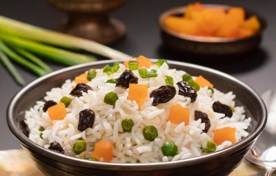 Tigela marrom com arroz colorido com passas, ervilhas e cenouras picadas.