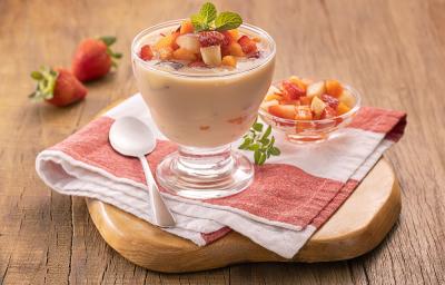 Foto em tons de vermelho da receita de taça cremosa de frutas servida em uma taça de vidro sobre um pano listrado com uma colher prateada e uma taça menor com pedaços de frutas ao lado. Tudo sobre uma tábua de madeira e há morangos ao fundo Foto em tons de vermelho da receita de taça cremosa de frutas servida em uma taça de vidro sobre um pano listrado com uma colher prateada e uma taça menor com pedaços de frutas ao lado. Tudo sobre uma tábua de madeira e há morangos ao fundo