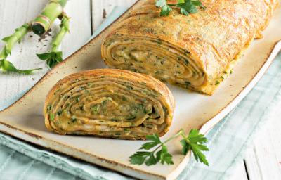 Fotografia em tons de verde em uma bancada de madeira clara com um recipiente retangular bem comprido e grande com a omelete em forma de rocambole. Fotografia em tons de verde em uma bancada de madeira clara com um recipiente retangular bem comprido e grande com a omelete em forma de rocambole.