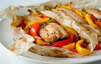Fotografia de um filé de peixe no papillote com legumes por baixo cortados em fatias. Na fotografia são dois papillotes de peixe com legumes, um do lado do outro sobre um prato branco de vidro. Fotografia de um filé de peixe no papillote com legumes por baixo cortados em fatias. Na fotografia são dois papillotes de peixe com legumes, um do lado do outro sobre um prato branco de vidro.