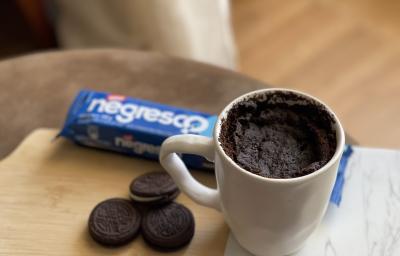 Foto de uma caneca branca contendo a receita de Bolo Negresco, sobre uma tábua com alguns Biscoitos Negresco soltos e um pacote em tom azul de Biscoito Negresco Foto de uma caneca branca contendo a receita de Bolo Negresco, sobre uma tábua com alguns Biscoitos Negresco soltos e um pacote em tom azul de Biscoito Negresco