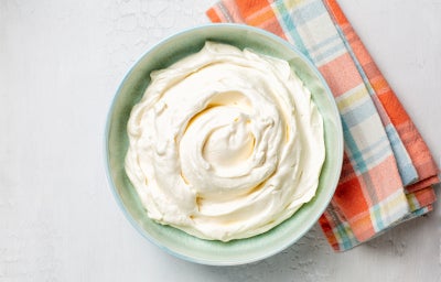 Pote verde claro com o recheio de Ninho Trufado cremoso sobre uma mesa branca com um paninho xadrez colorido.