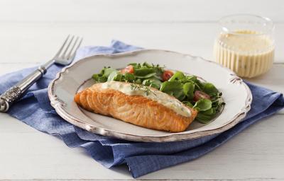 fotografia em tons de branco e azul de uma bancada branca vista de frente, contém um pano azul, um prato redondo branco com um pedaço de salmão com creme branco por cima e folhas com fatias de tomate cereja para acompanhar. Ao lado um garfo para servir fotografia em tons de branco e azul de uma bancada branca vista de frente, contém um pano azul, um prato redondo branco com um pedaço de salmão com creme branco por cima e folhas com fatias de tomate cereja para acompanhar. Ao lado um garfo para servir