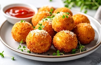 Em cima de uma mesa, prato cinza com porção de bolinho dourado e crocante, polvilhado com queijo ralado.
