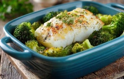 Em cima de uma mesa, refratário azul escuro com posta de bacalhau e floretes de brócolis. Em cima de uma mesa, refratário azul escuro com posta de bacalhau e floretes de brócolis.