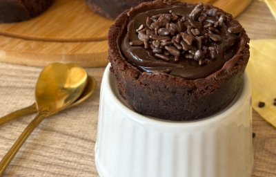 Imagem de uma torta pequena redonda com massa de chocolate e recheio sobre um recipiente branco.