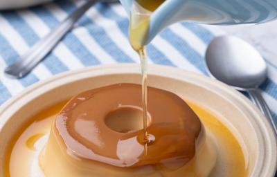 Fotografia de um mini pudim sore um prato raso de cor clara. Por cima do pudim tem uma calda de caramelo caindo de uma jarra pequena. Fotografia de um mini pudim sore um prato raso de cor clara. Por cima do pudim tem uma calda de caramelo caindo de uma jarra pequena.