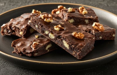 Em cima de uma mesa, barra com pedaços de massa com nozes, chocolate derretido e nozes picadas. Em cima de uma mesa, barra com pedaços de massa com nozes, chocolate derretido e nozes picadas.